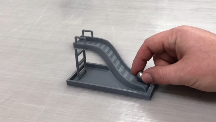 A hand placing a metal ball at the base of a 3D printed slide